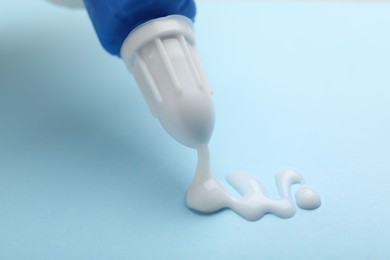 Photo of Applying glue from bottle on light blue background, closeup