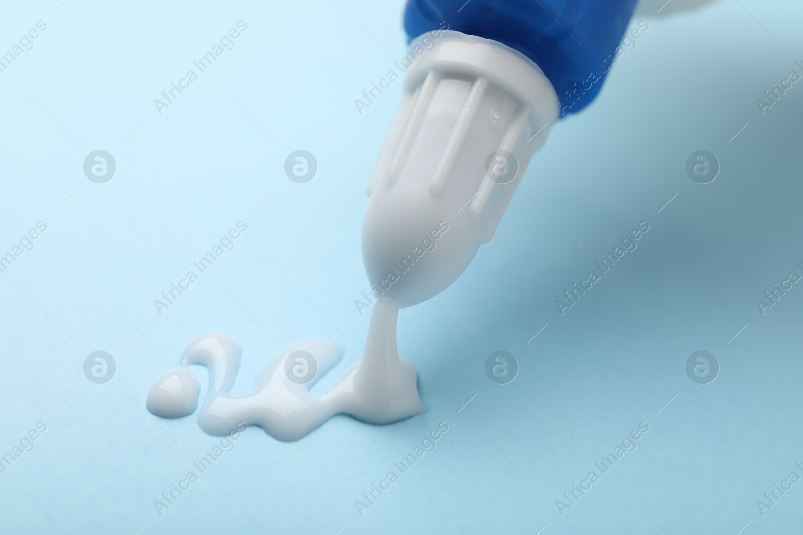 Photo of Applying glue from bottle on light blue background, closeup