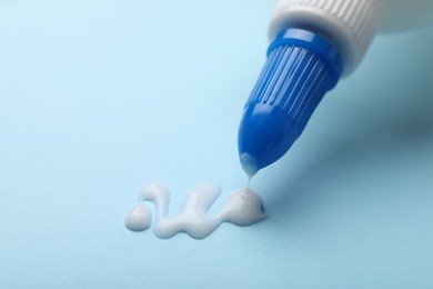 Photo of Applying glue from bottle on light blue background, closeup. Space for text