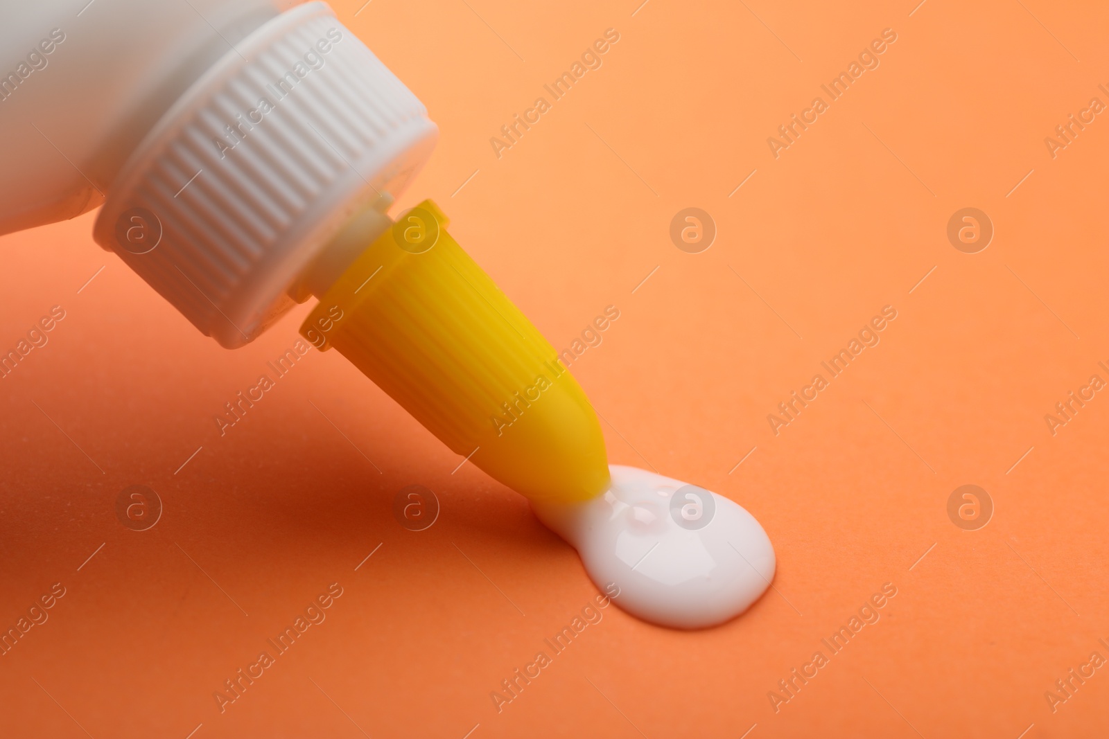 Photo of Applying glue from bottle on orange background, closeup. Space for text