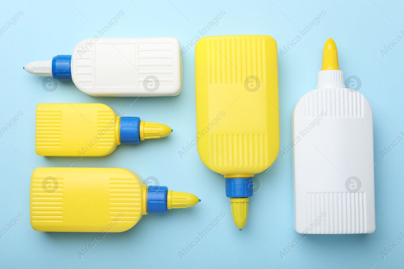 Photo of Bottles of glue on light blue background, flat lay