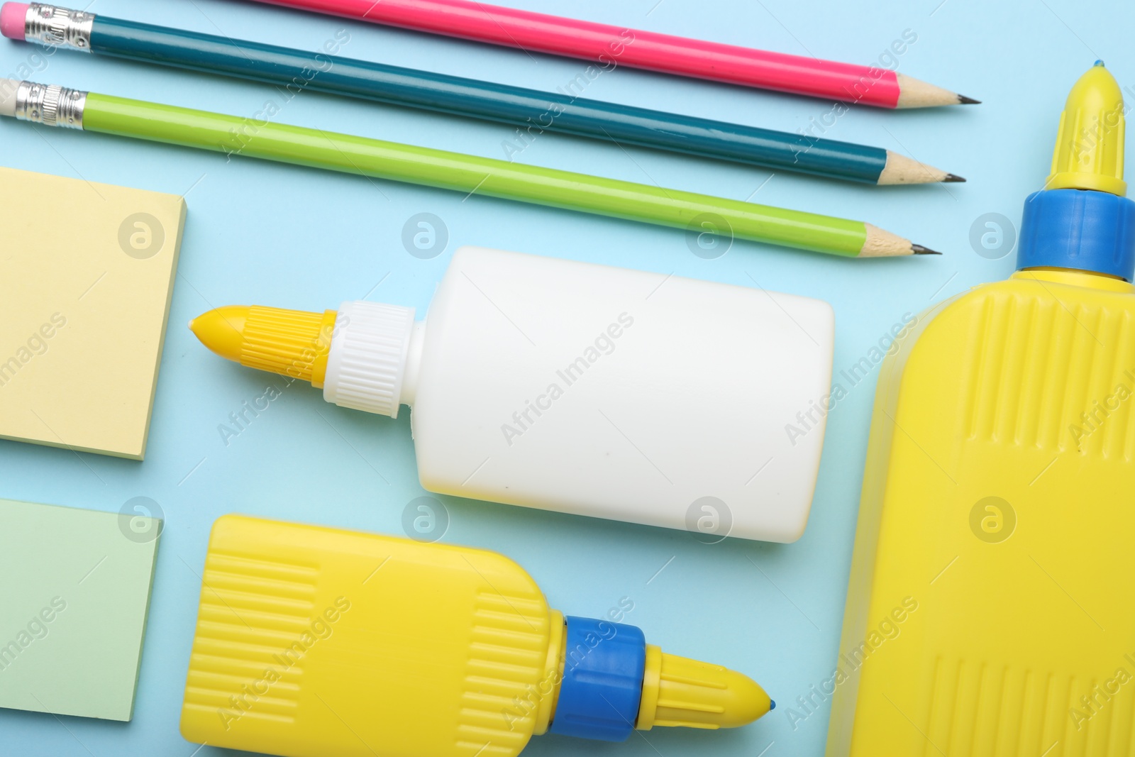 Photo of Bottles of glue, pencils and notes on light blue background, flat lay