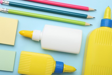 Photo of Bottles of glue, pencils and notes on light blue background, flat lay