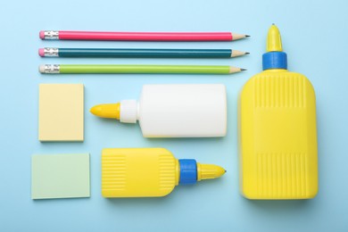 Photo of Bottles of glue, pencils and notes on light blue background, flat lay