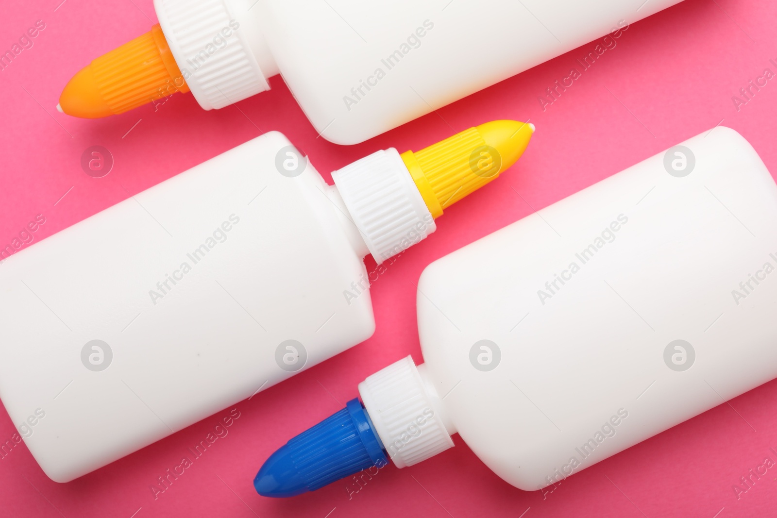 Photo of Bottles of glue on pink background, flat lay