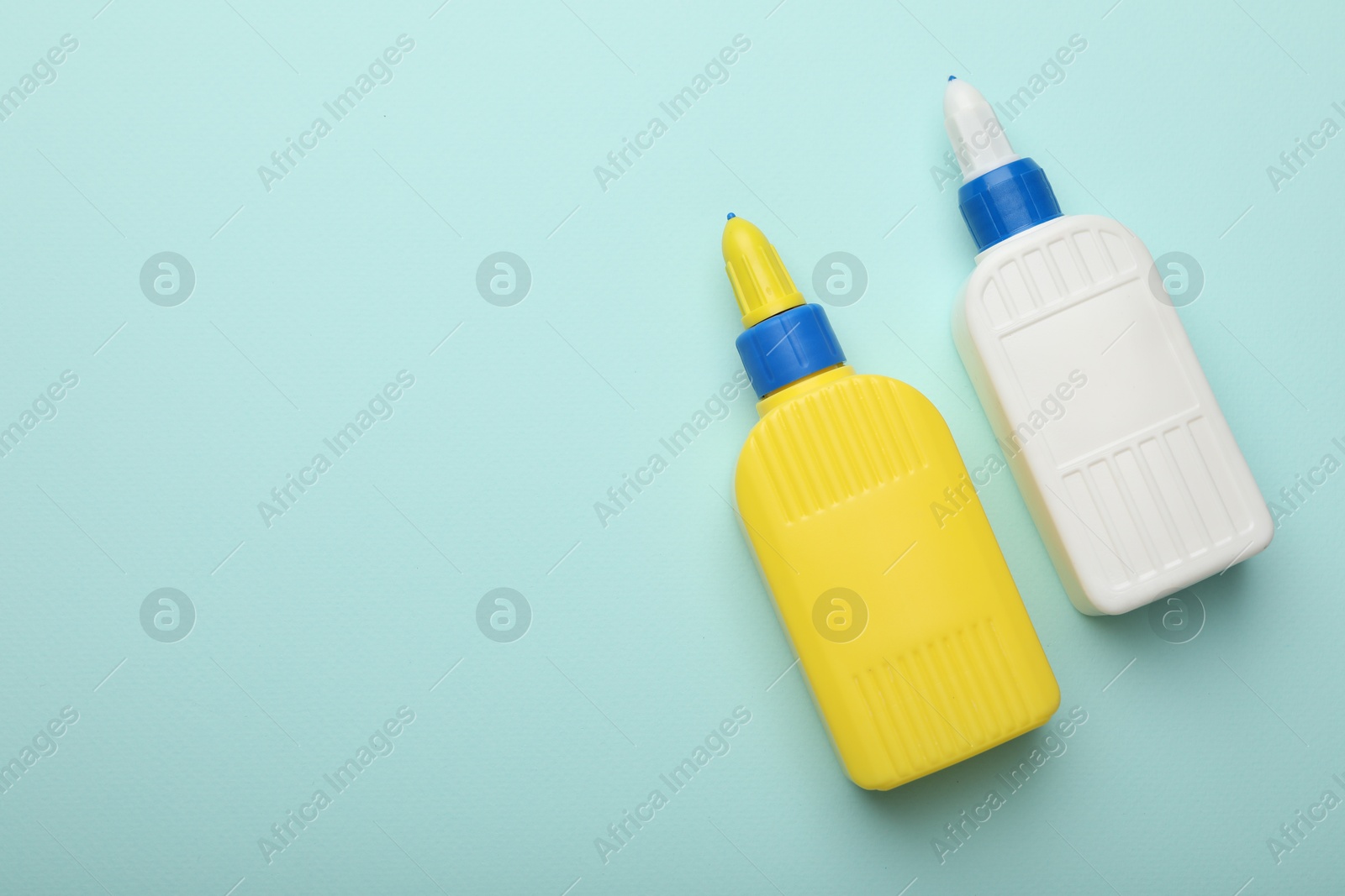 Photo of Bottles of glue on light blue background, top view. Space for text