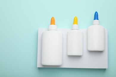 Photo of Bottles of glue on light blue background, flat lay. Space for text