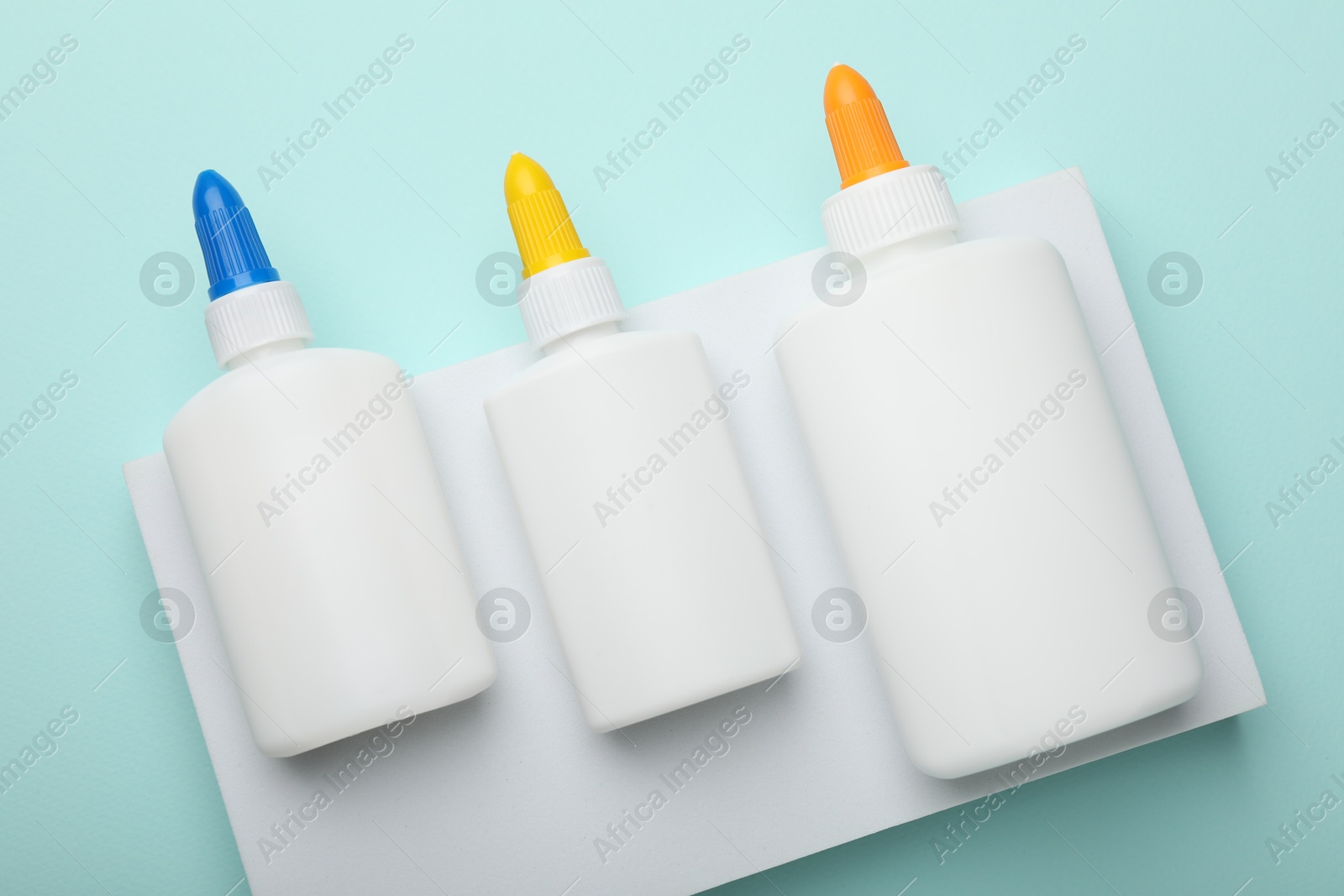 Photo of Bottles of glue on light blue background, top view