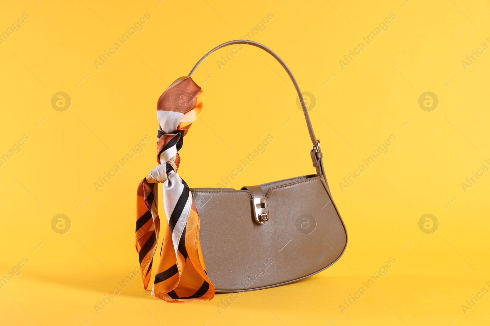 Photo of Stylish brown leather bag with handkerchief on yellow background