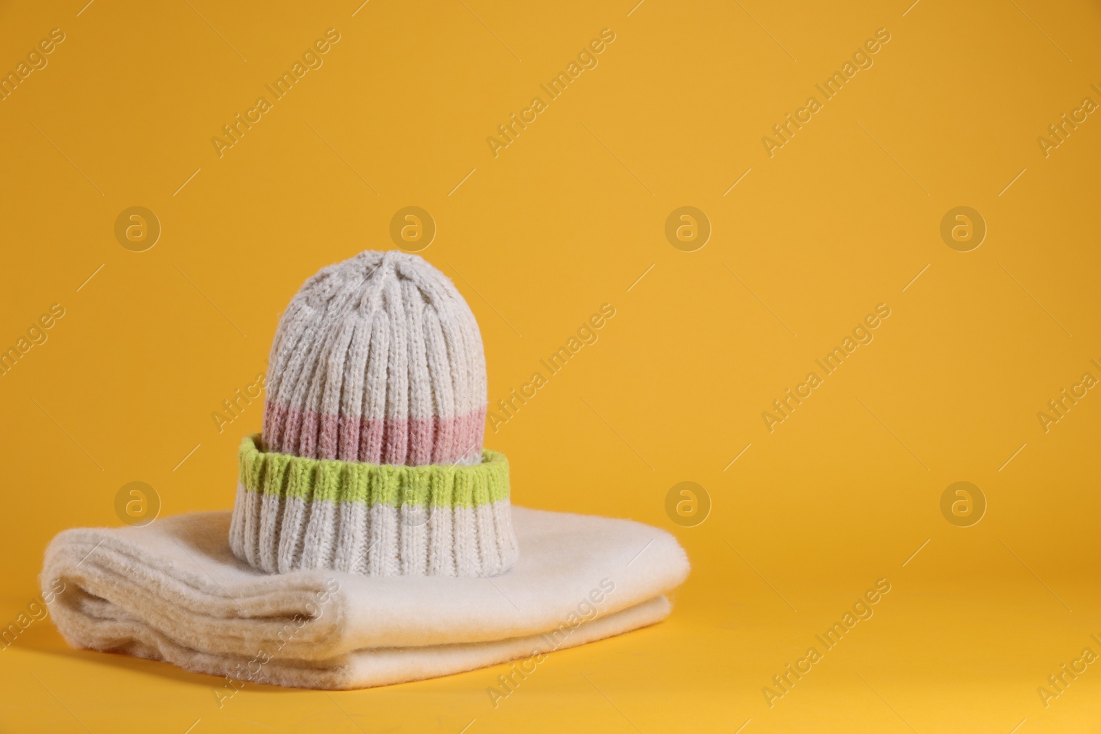 Photo of Stylish knitted hat and warm scarf on yellow background, space for text