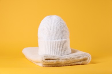 Photo of Stylish knitted hat and warm scarf on yellow background