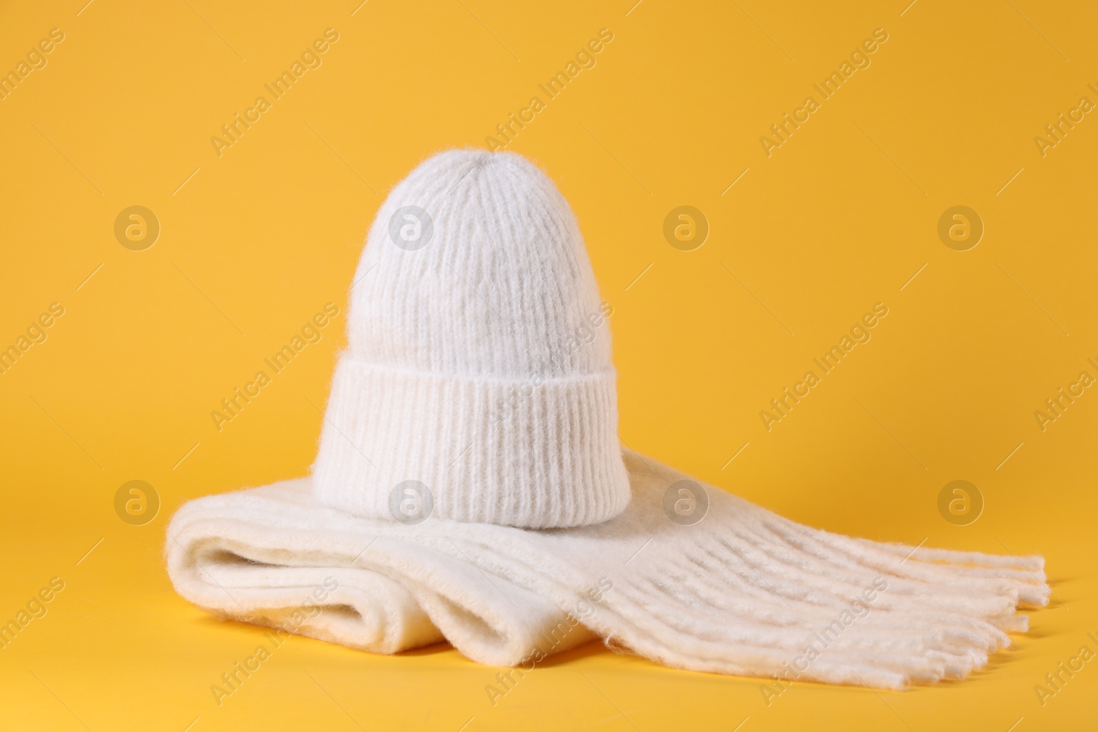 Photo of Stylish knitted hat and warm scarf on yellow background