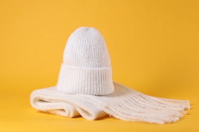 Photo of Stylish knitted hat and warm scarf on yellow background