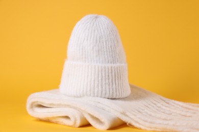 Photo of Stylish knitted hat and warm scarf on yellow background