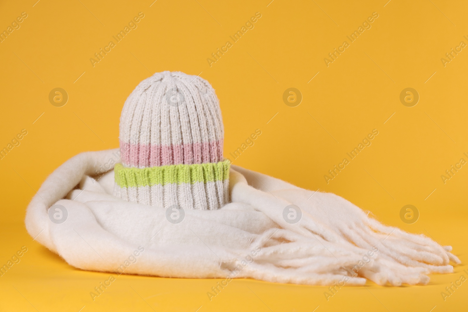 Photo of Stylish knitted hat and warm scarf on yellow background