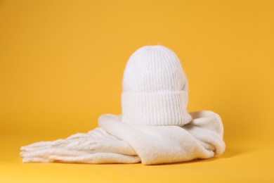 Photo of Stylish knitted hat and warm scarf on yellow background