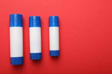 Photo of Sticks of glue on red background, flat lay. Space for text