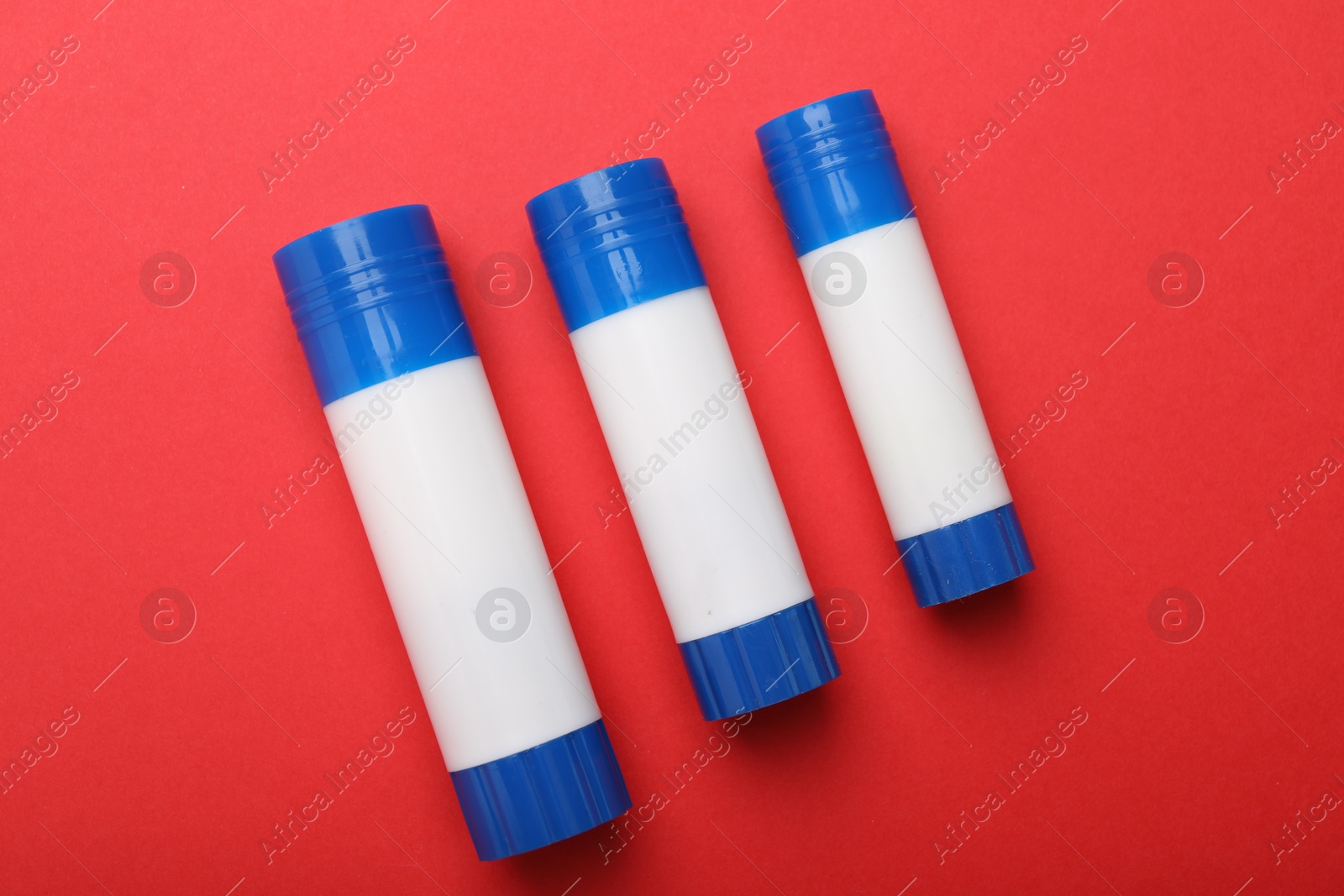 Photo of Sticks of glue on red background, flat lay