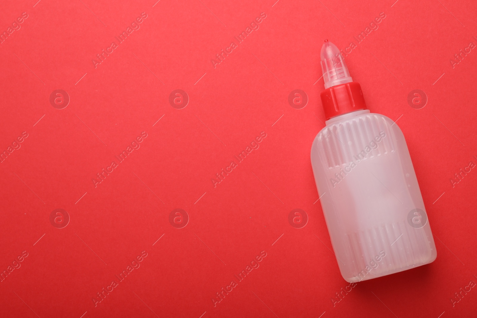 Photo of Bottle of glue on red background, top view. Space for text