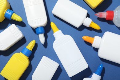 Photo of Bottles of glue on blue background, flat lay