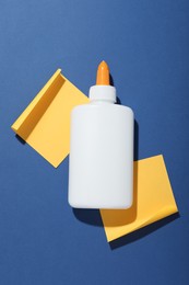 Photo of Bottle of glue and notes on blue background, flat lay