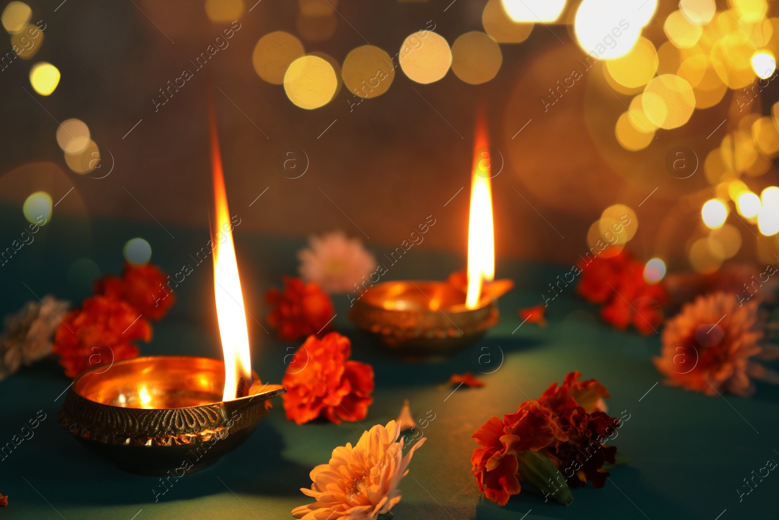 Image of Diwali celebration. Diya lamps and beautiful flowers on teal table, closeup. Bokeh effect