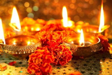 Image of Diwali celebration. Diya lamps and beautiful marigold flowers on patterned surface, closeup. Bokeh effect