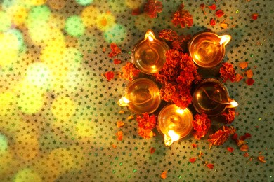 Image of Diwali celebration. Diya lamps and beautiful marigold flowers on patterned surface, flat lay. Bokeh effect