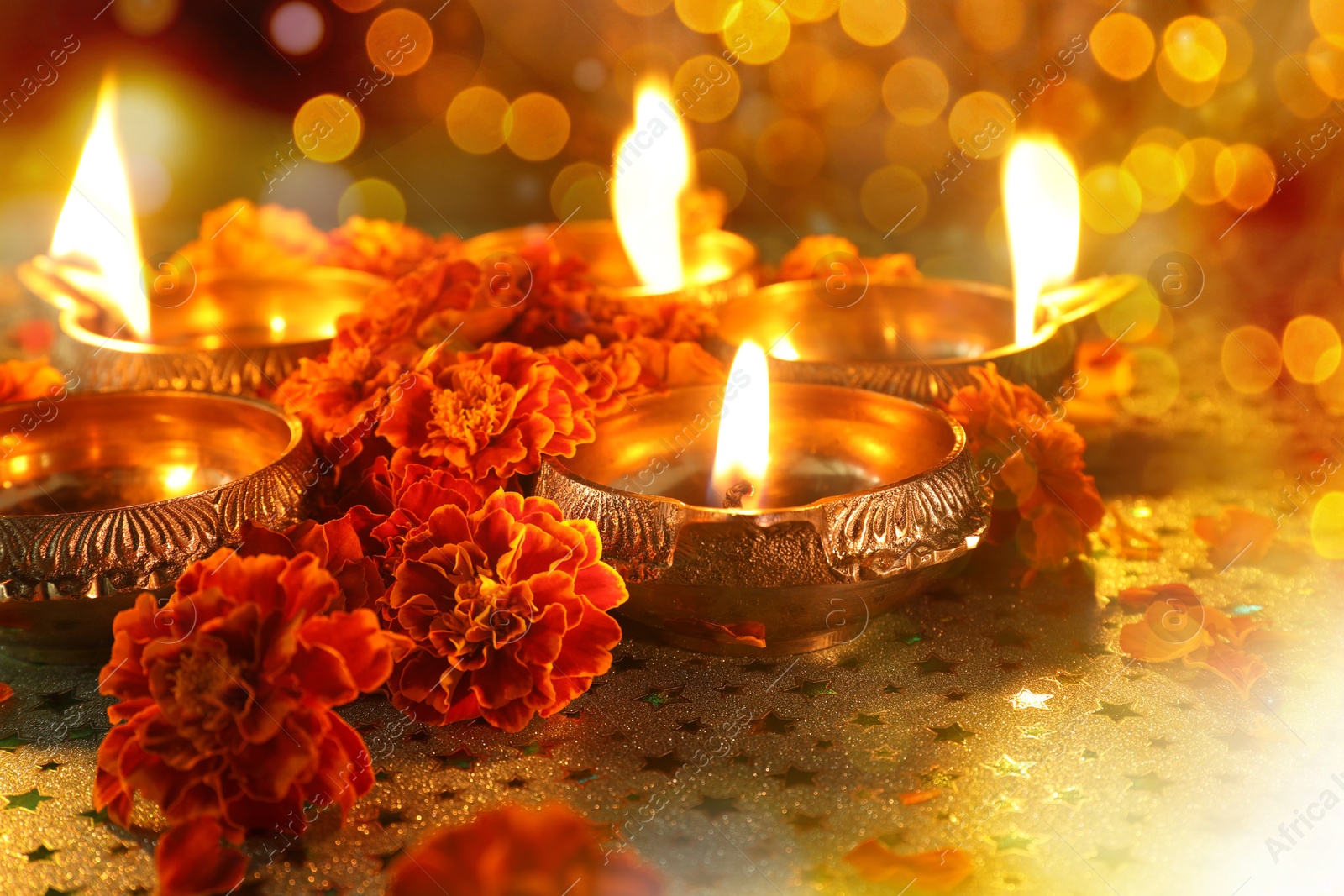 Image of Diwali celebration. Diya lamps and beautiful marigold flowers on patterned surface, closeup. Bokeh effect