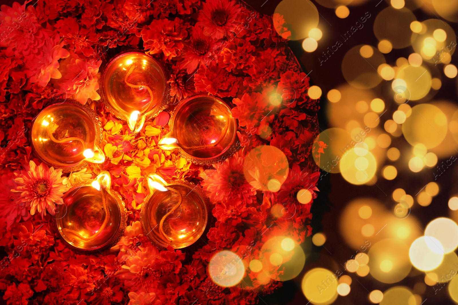 Image of Diwali celebration. Diya lamps and beautiful flowers on dark background, top view. Bokeh effect