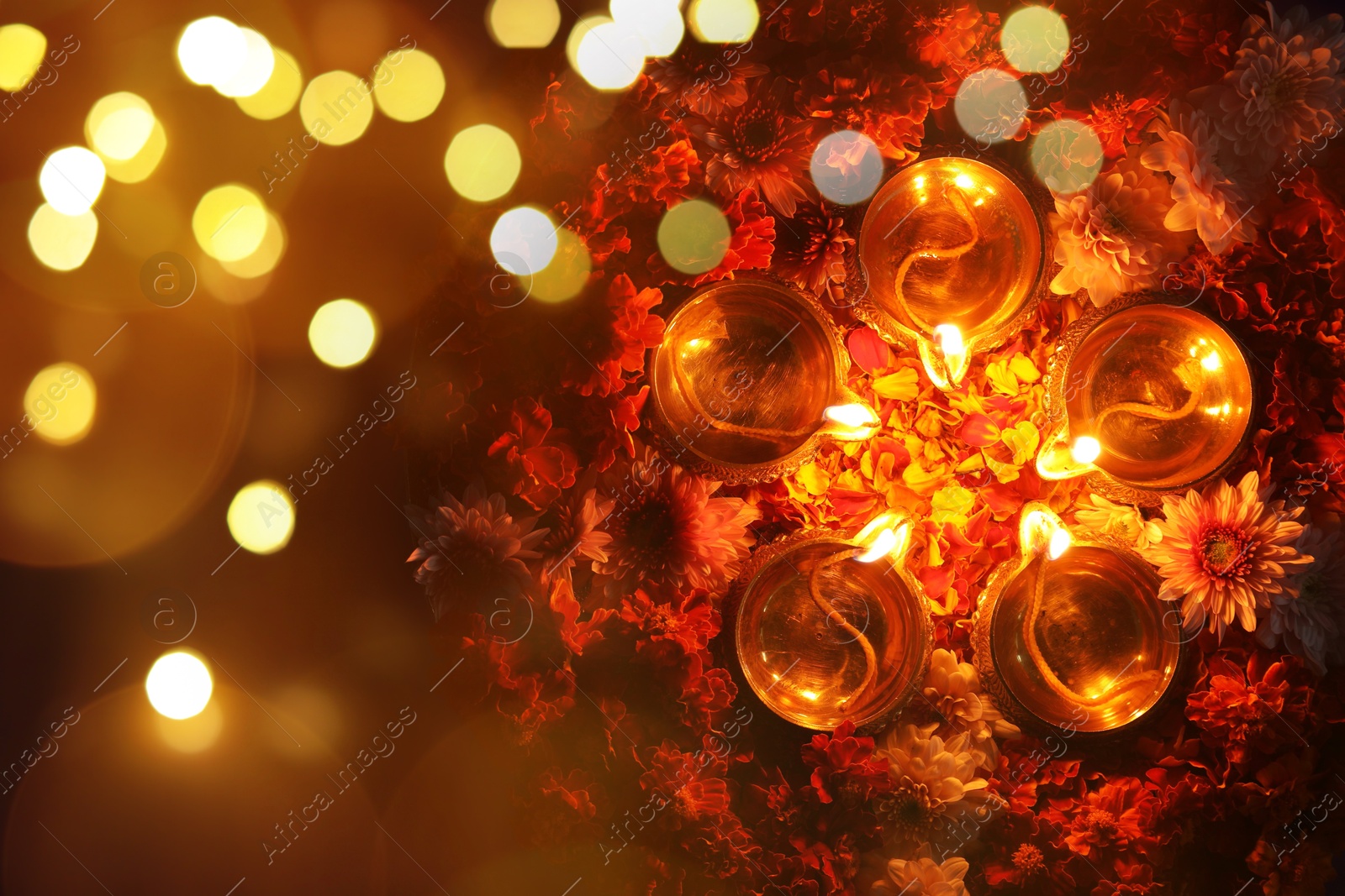 Image of Diwali celebration. Diya lamps and beautiful flowers on dark background, top view. Bokeh effect