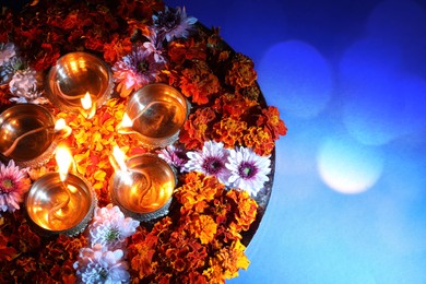 Image of Diwali celebration. Diya lamps and beautiful flowers on blue background, top view. Space for text. Bokeh effect