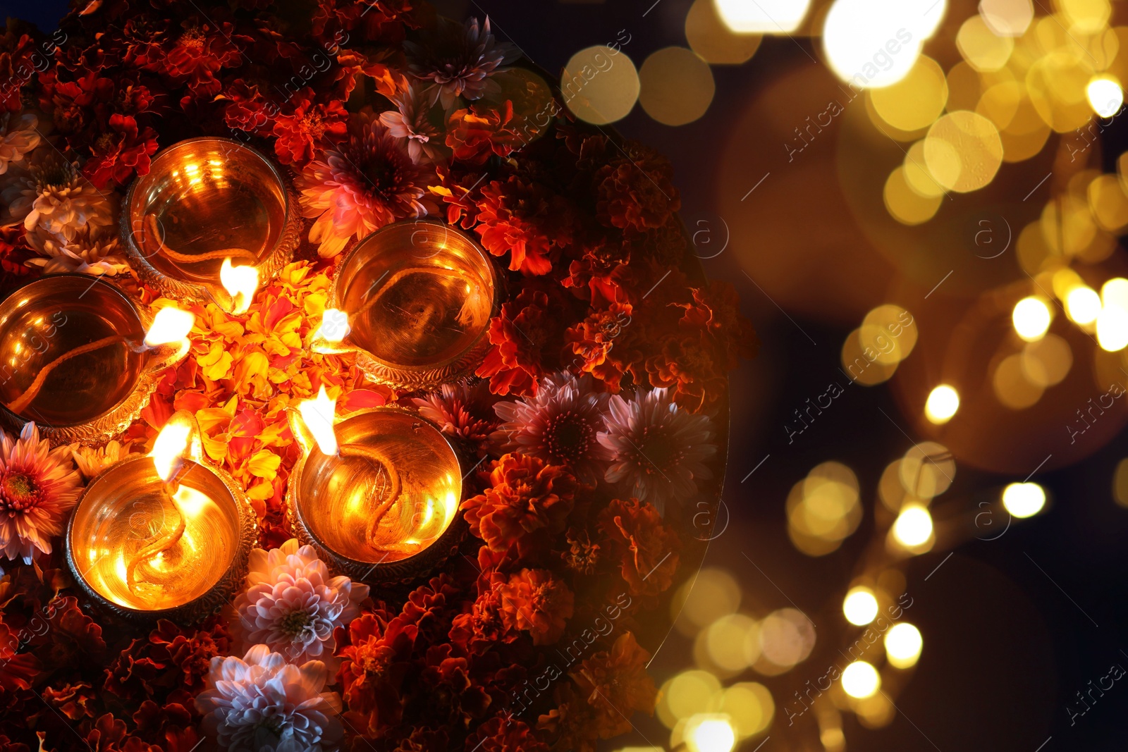 Image of Diwali celebration. Diya lamps and beautiful flowers on dark background, top view. Bokeh effect