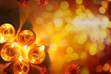 Image of Diwali celebration. Diya lamps and beautiful flowers on background with bokeh effect, top view