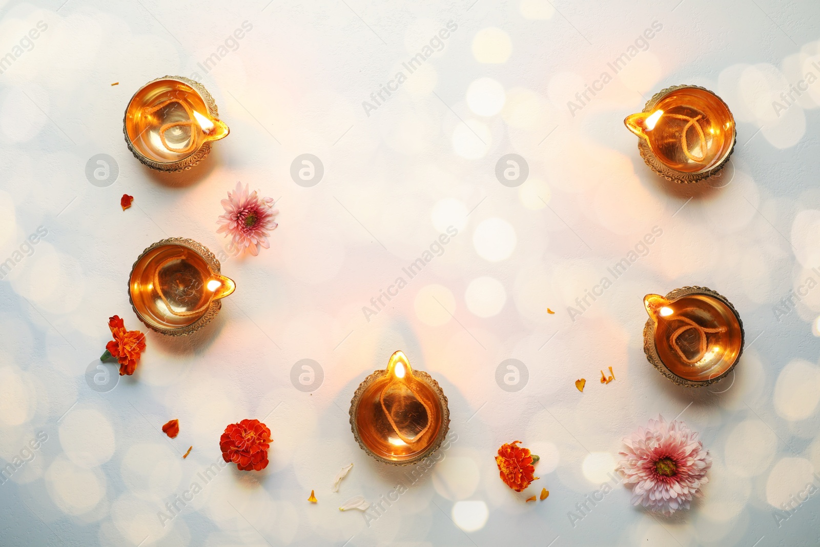 Image of Diwali celebration. Diya lamps and beautiful flowers on light surface, flat lay. Space for text. Bokeh effect