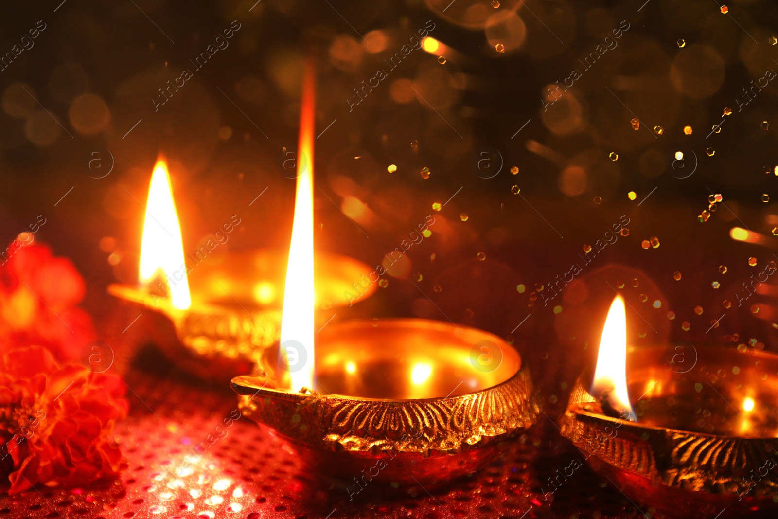 Image of Diwali celebration. Diya lamps and beautiful flowers on dark background, closeup. Bokeh effect