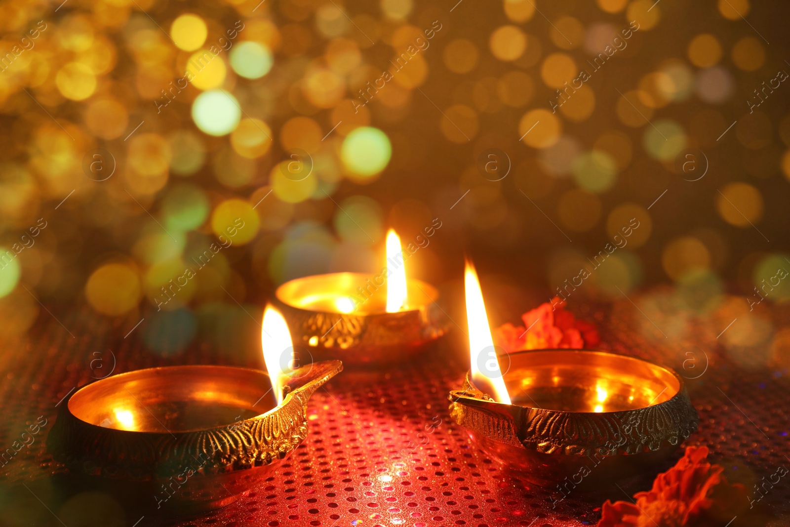 Image of Diwali celebration. Diya lamps and beautiful flowers on golden background, closeup. Bokeh effect