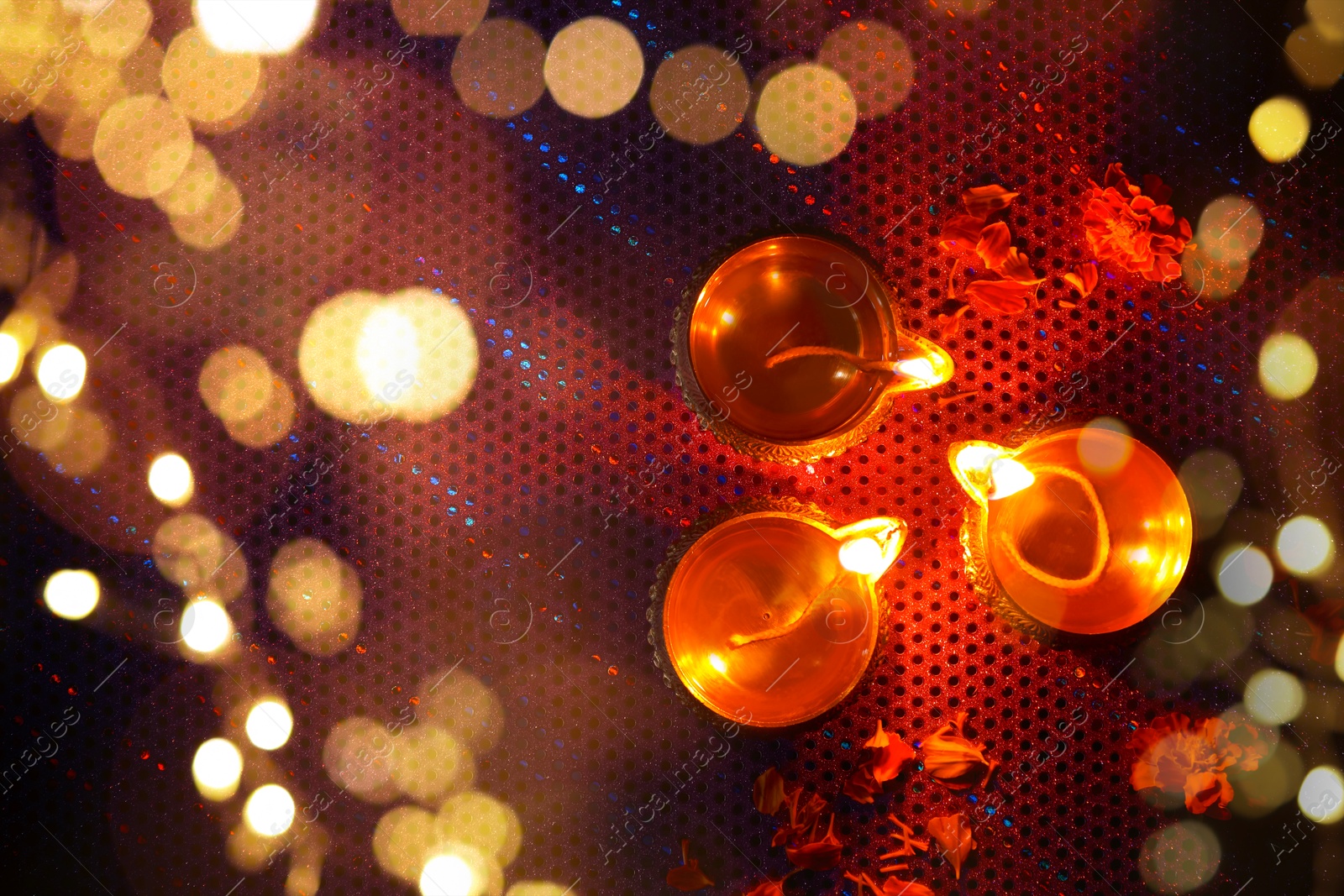 Image of Diwali celebration. Diya lamps and beautiful flowers on dark background, top view. Bokeh effect