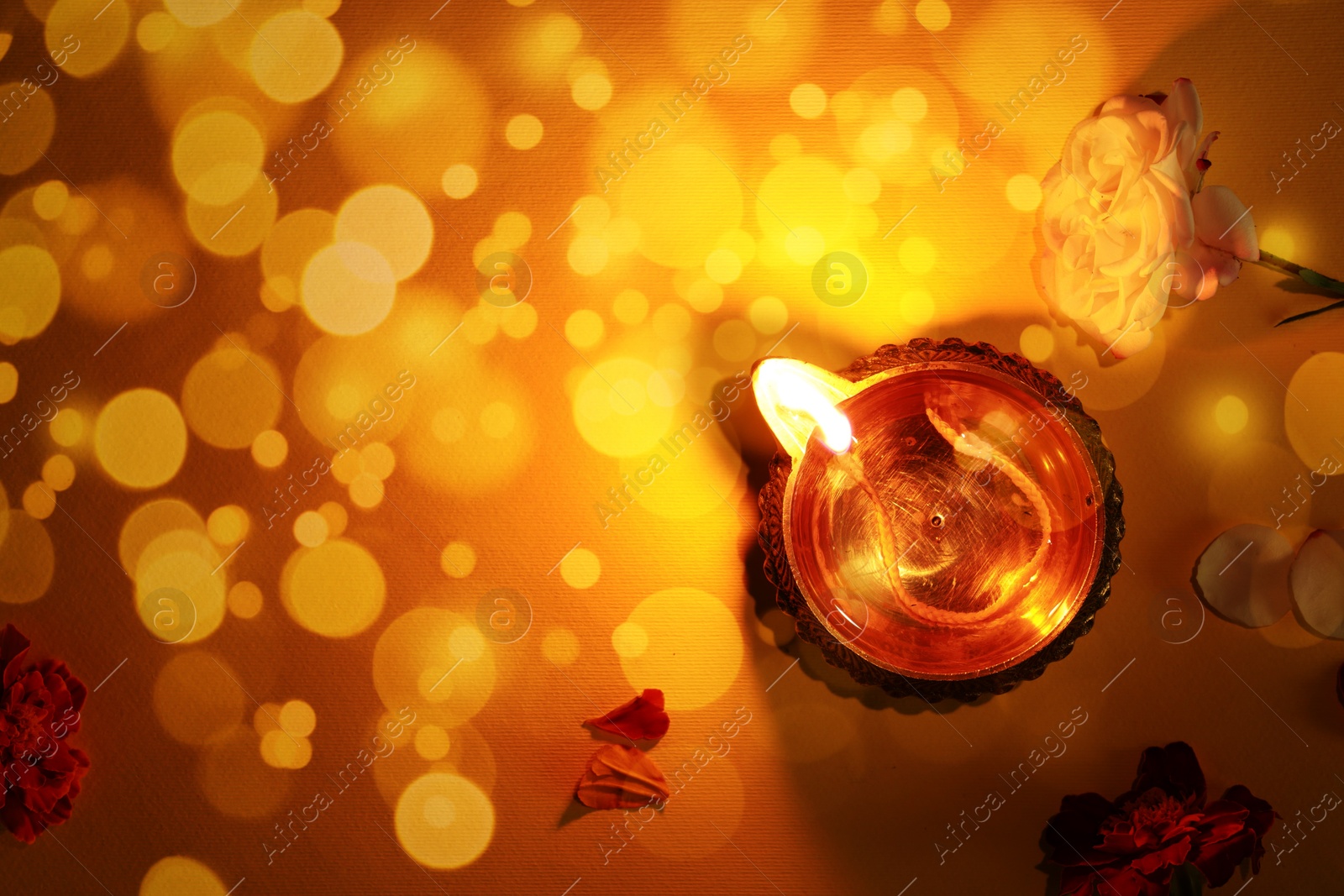 Image of Diwali celebration. Diya lamp and beautiful flowers on orange background, top view. Space for text. Bokeh effect