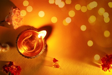 Image of Diwali celebration. Diya lamp and beautiful flowers on orange background, top view. Space for text. Bokeh effect