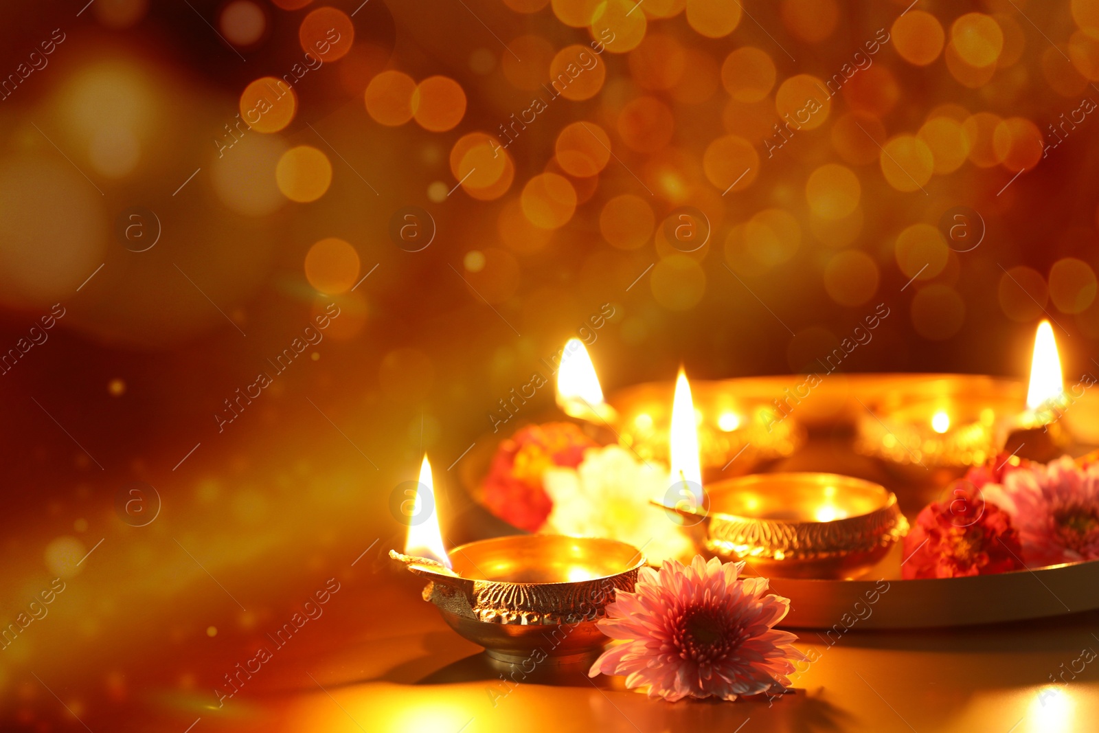 Image of Diwali celebration. Diya lamps and beautiful flowers on color background, closeup. Space for text. Bokeh effect