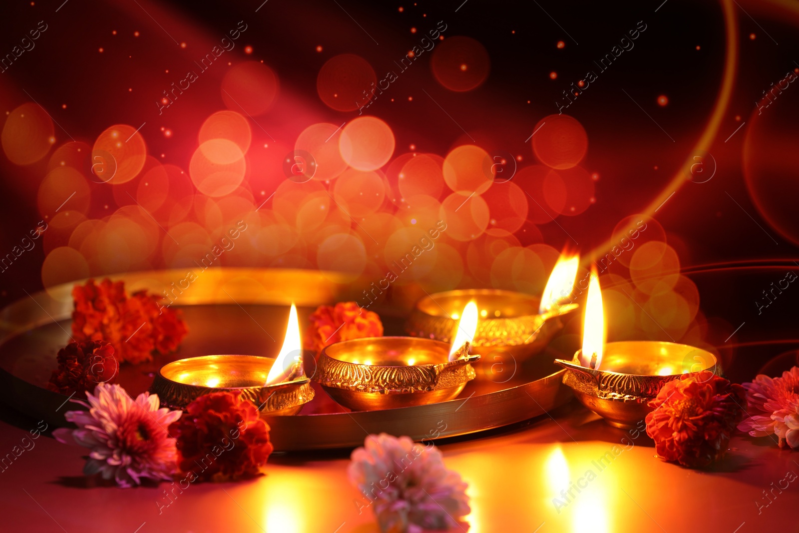 Image of Diwali celebration. Diya lamps and beautiful flowers on color background, closeup. Bokeh effect