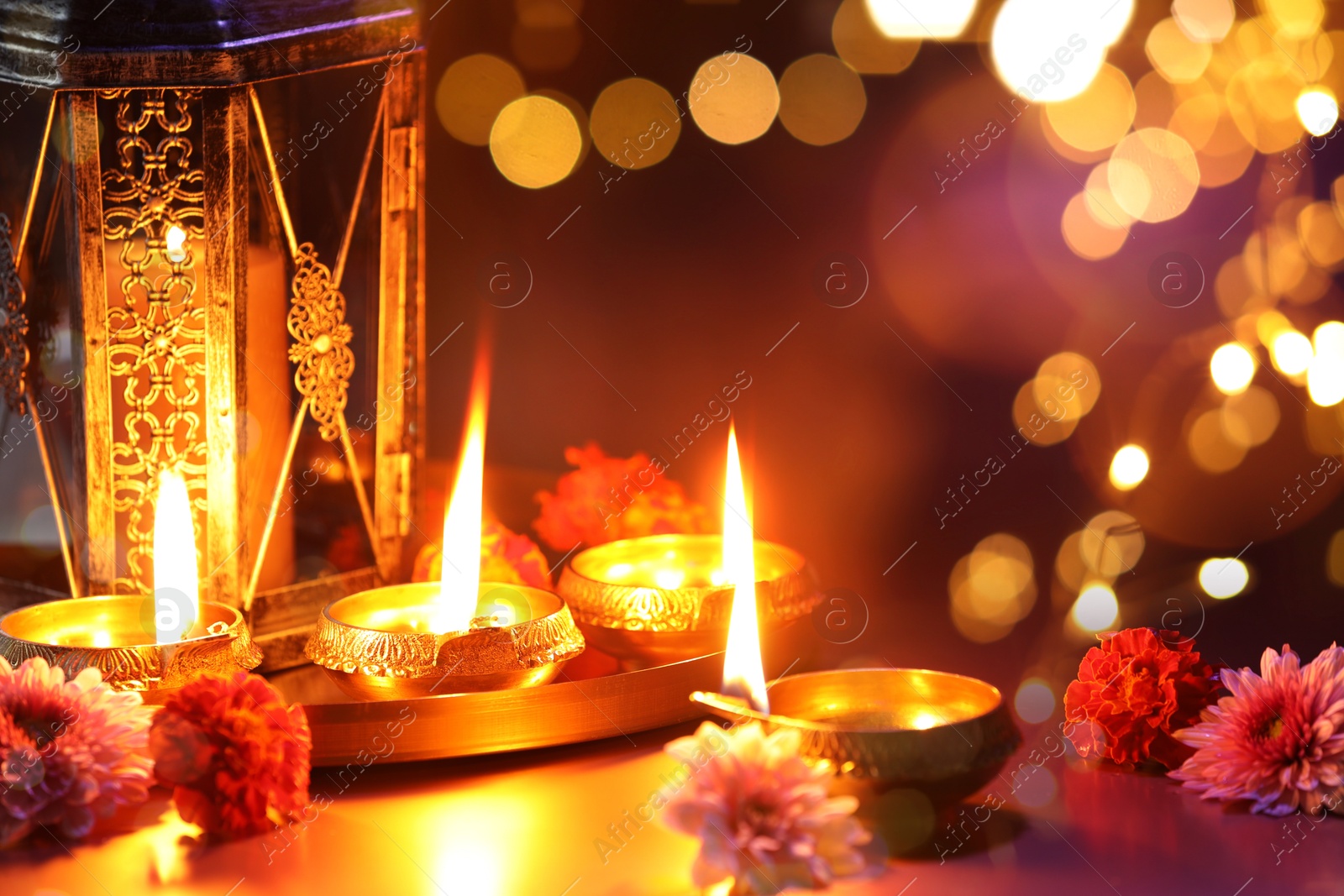 Image of Diwali celebration. Diya lamps and beautiful flowers on color background, closeup. Bokeh effect