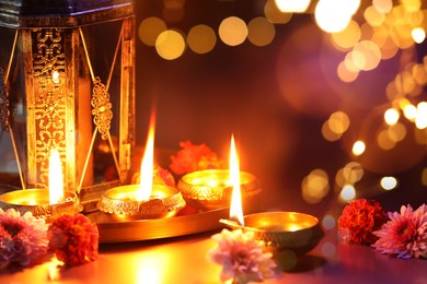 Image of Diwali celebration. Diya lamps and beautiful flowers on color background, closeup. Bokeh effect