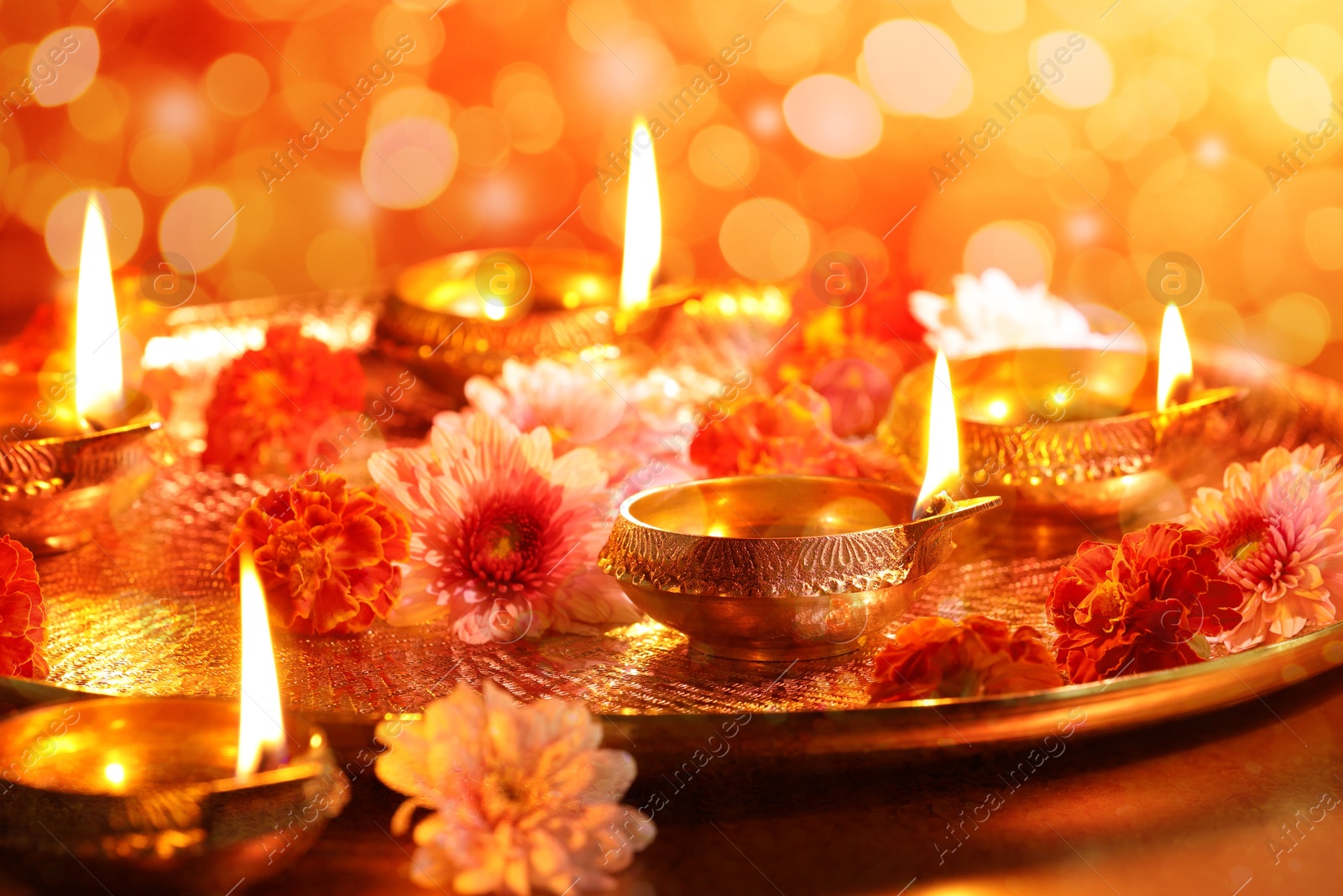 Image of Diwali celebration. Diya lamps and beautiful flowers on color background, closeup. Bokeh effect