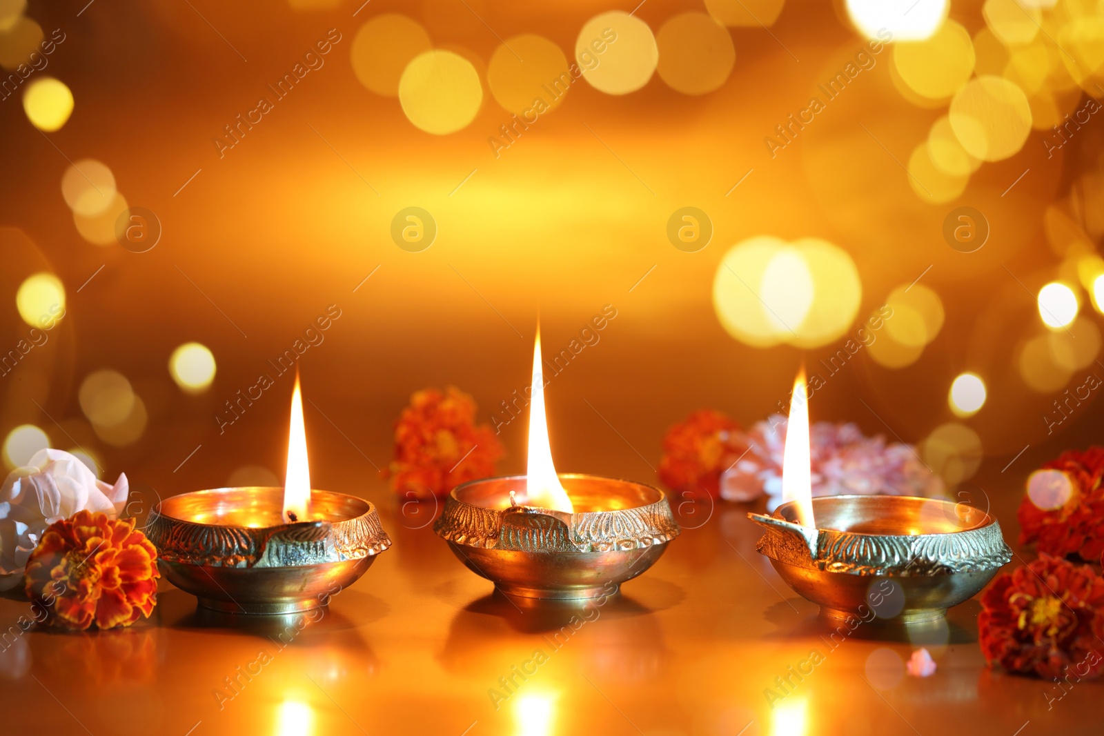 Image of Diwali celebration. Diya lamps and beautiful flowers on golden background, space for text. Bokeh effect