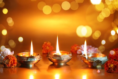 Image of Diwali celebration. Diya lamps and beautiful flowers on golden background, space for text. Bokeh effect