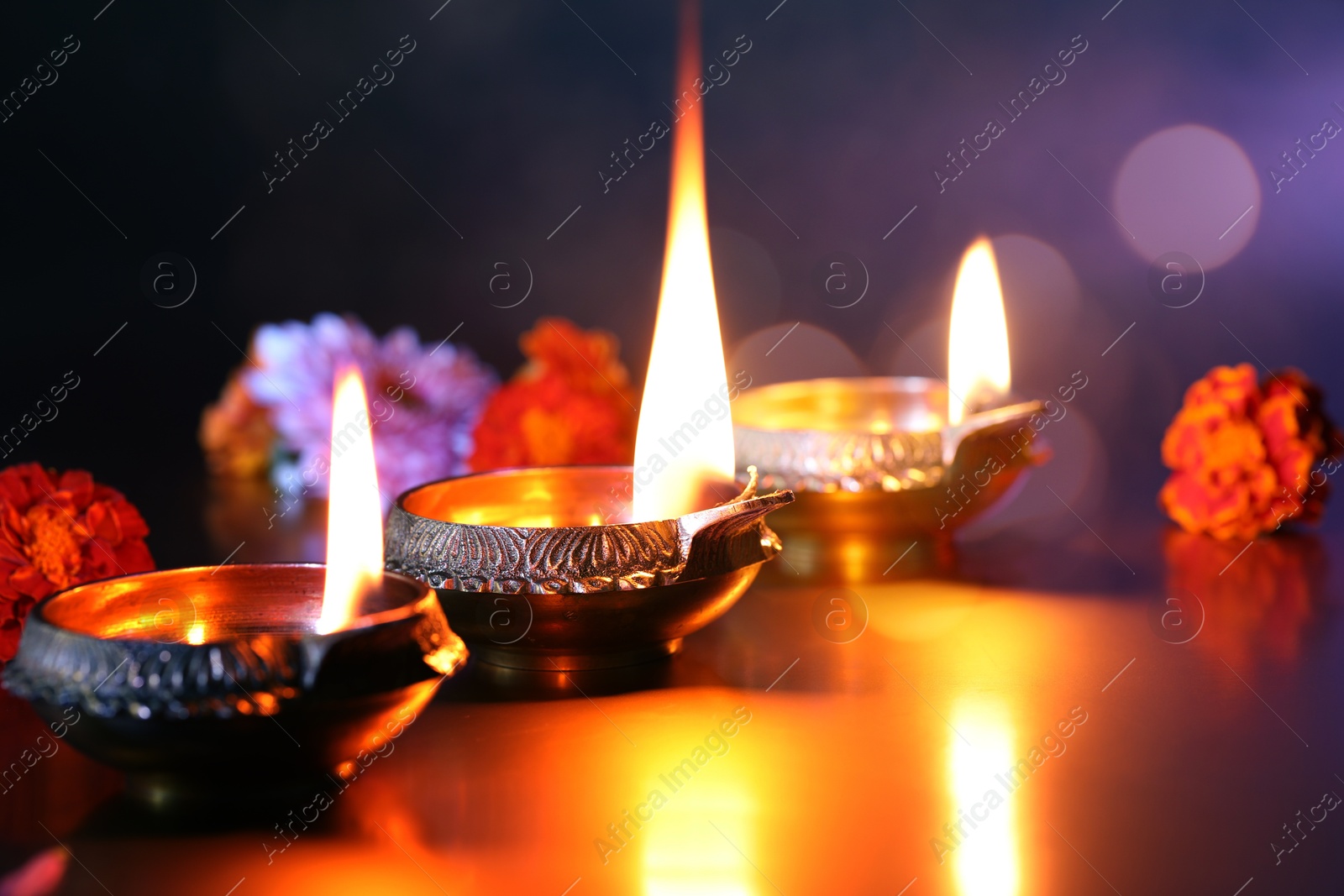 Image of Diwali celebration. Diya lamps and beautiful flowers on color background, closeup. Bokeh effect