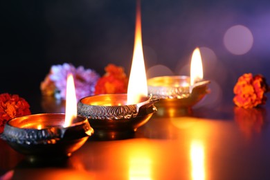 Image of Diwali celebration. Diya lamps and beautiful flowers on color background, closeup. Bokeh effect