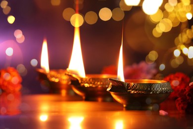 Image of Diwali celebration. Diya lamps and beautiful flowers on color background, closeup. Bokeh effect